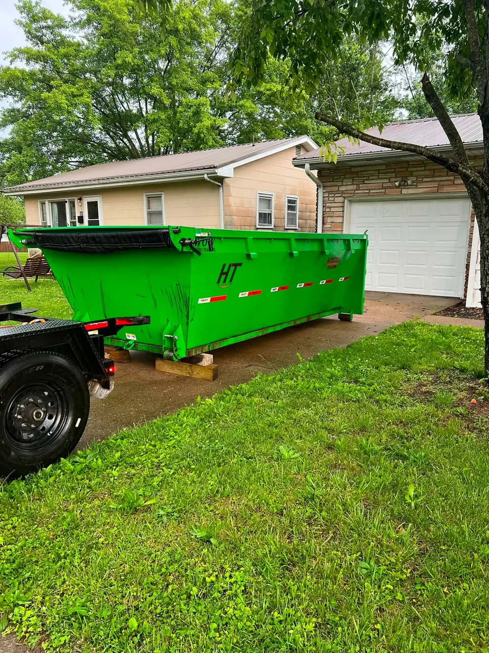Green roll-off dumpster in a residential driveway next to a garage