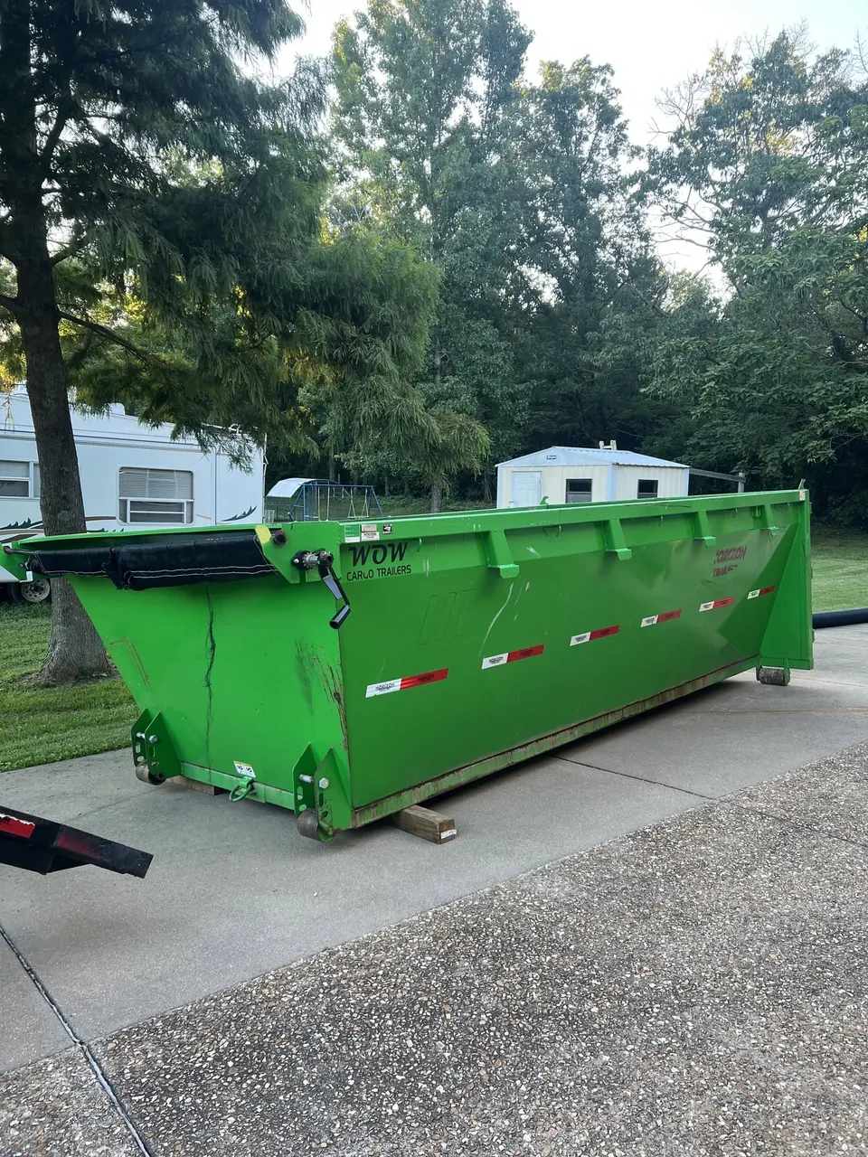 Green 14-yard roll-off dumpster set on wooden boards on a concrete driveway